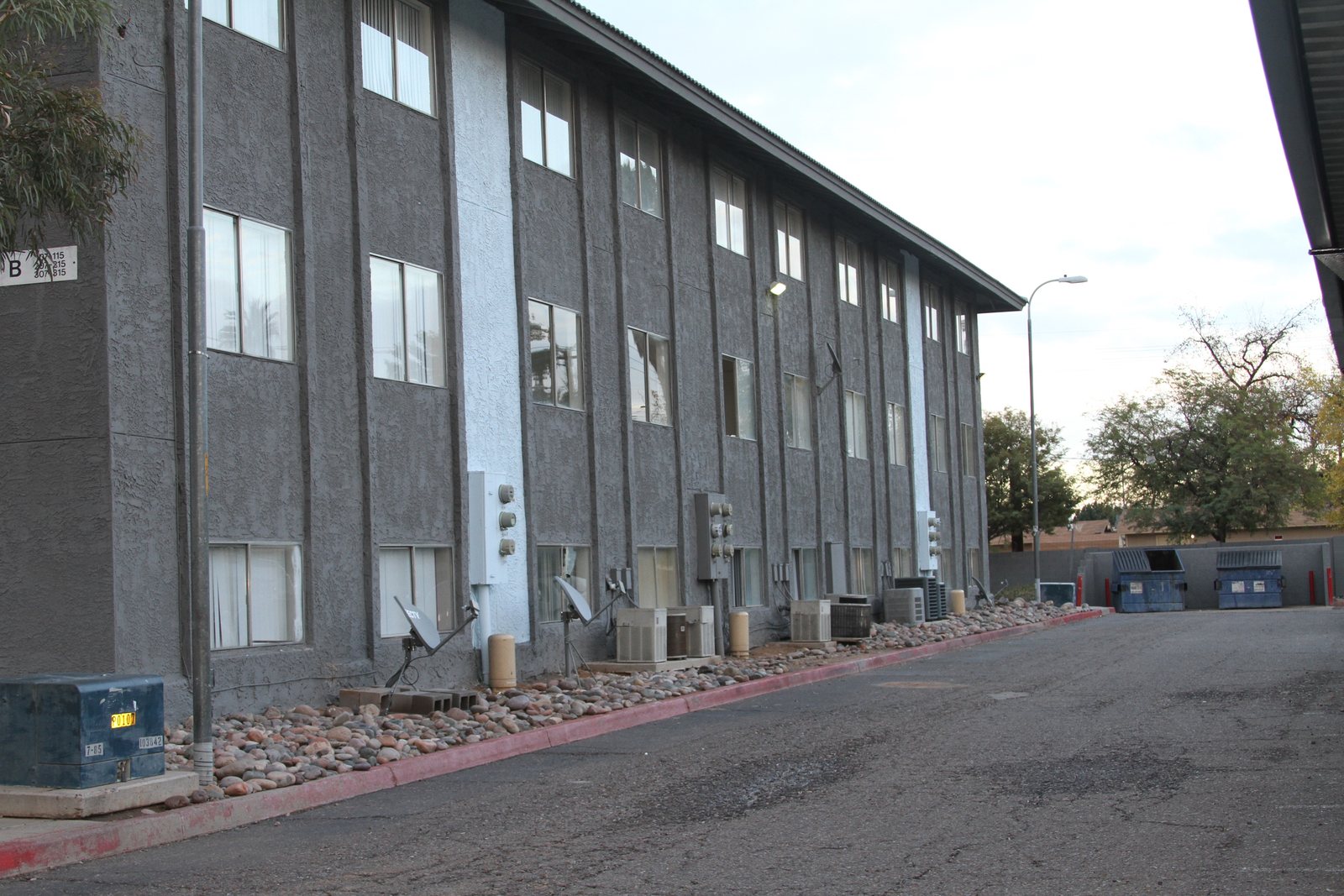 Rear elevation of a three-story Arizona apartment building painted by Happy Brush Painters &mdash; two-tone grey stucco, satellite dishes and utility banks worked around