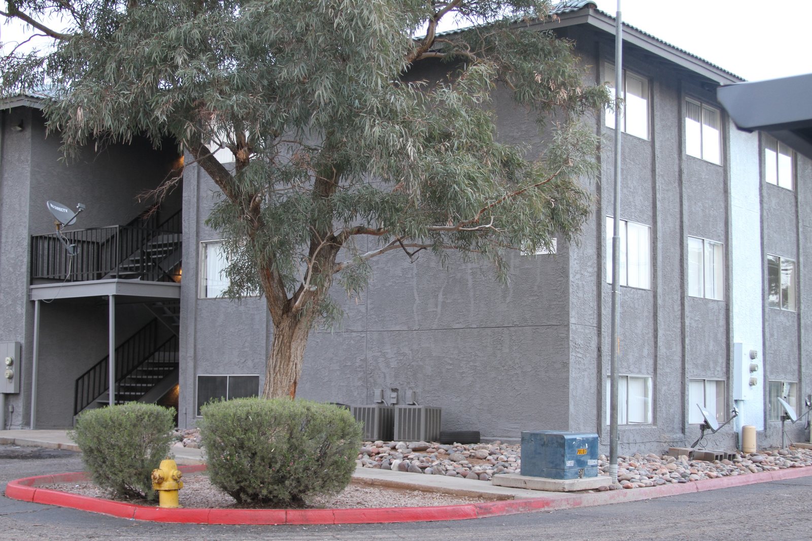 Corner elevation of the apartment community showing the two-grey scheme and ground-floor utility equipment