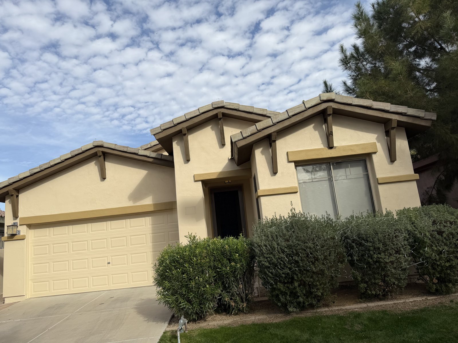 Exterior repaint on a single-story Arizona home &mdash; cream stucco body with gold trim bands, wood corbels and a tile roof