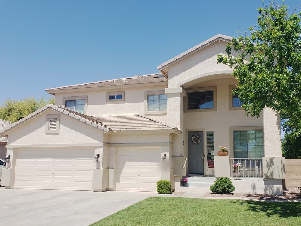 Two-story Arizona home with a three-car garage painted by Happy Brush Painters &mdash; light neutral stucco with matching trim and white garage doors