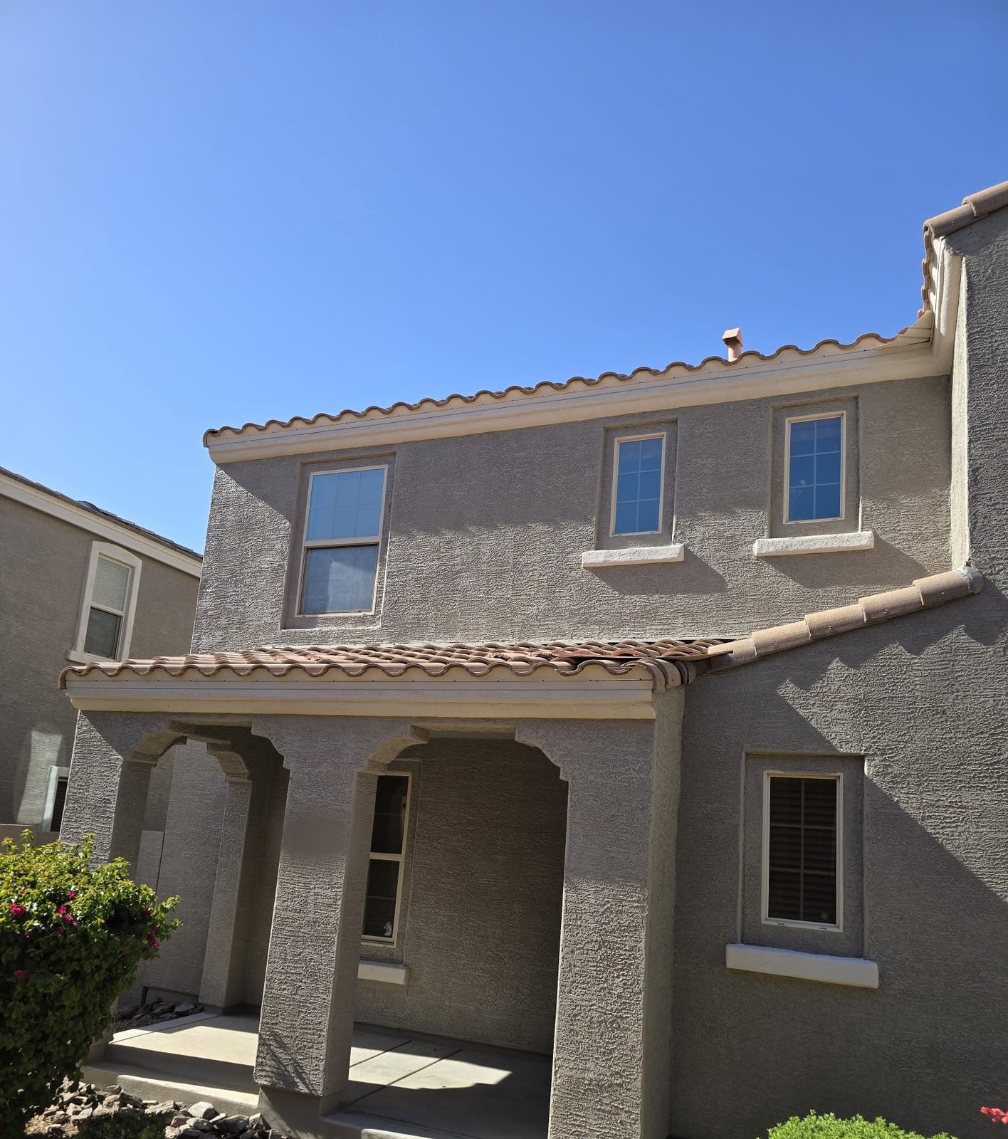 Two-story Arizona home painted by Happy Brush Painters &mdash; warm grey stucco with cream window sills and fascia, tile roof and a covered entry porch