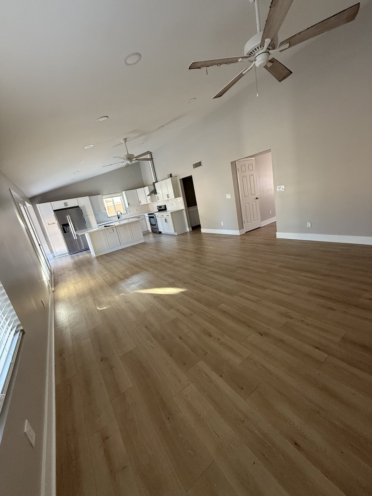 Open-plan living room and kitchen with vaulted ceiling, repainted in a warm neutral over wood-look floors
