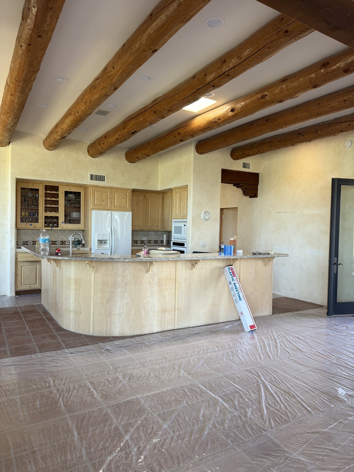 Kitchen with exposed wood beams fully masked and floors sheeted mid-repaint