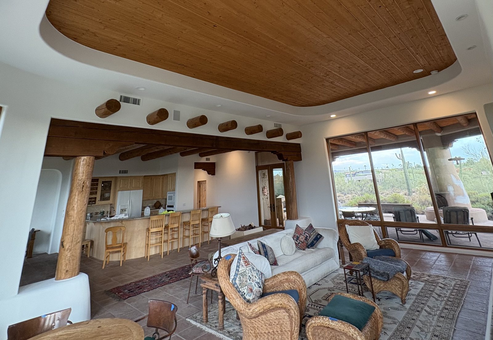 Great room of a custom Arizona home &mdash; white painted walls cut cleanly against a stained wood plank ceiling, vigas and log posts